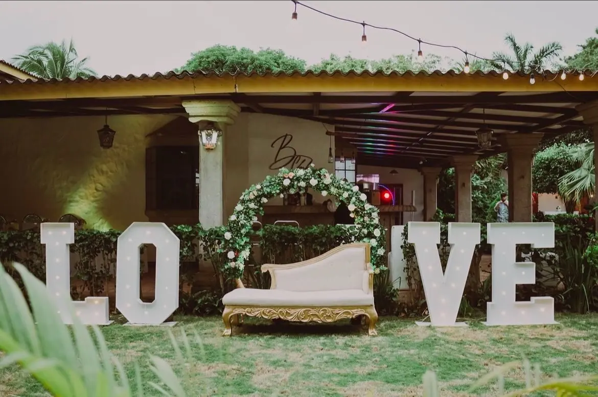 Montaje en el Salón Garden con arco de flores, sofá dorado y letras LOVE