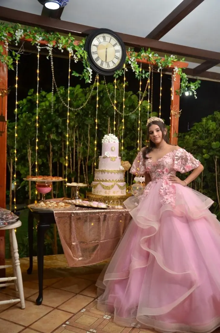 Quinceañera con vestido rosa junto a la mesa del pastel